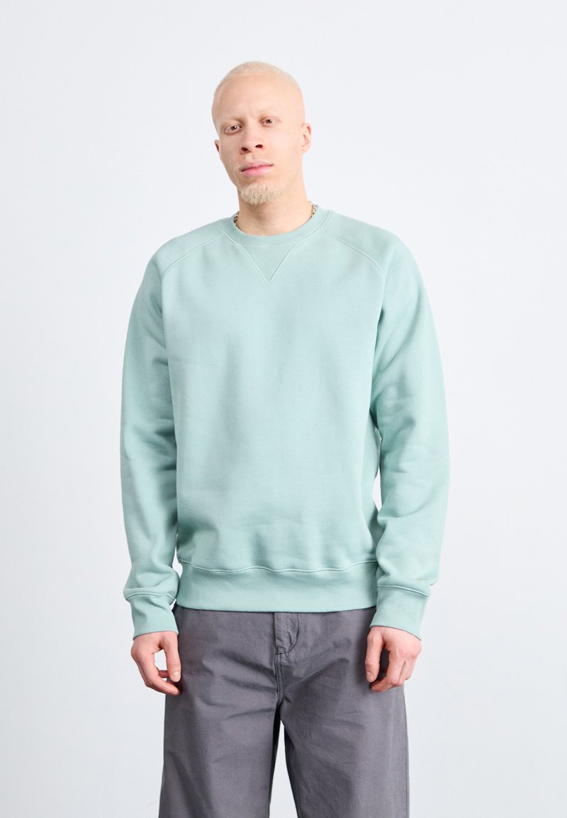 Licht mintgroene sweatshirt gemaakt van zacht stof met een ronde hals, geribbelde manchetten en een relaxte pasvorm. Draagt bij grijze broek.