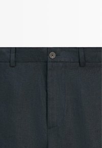 Pantalon gris foncé avec une fermeture à un bouton et des passants pour ceinture, montrant la taille et la partie avant de la braguette.