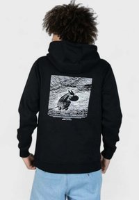 Mustat hupparitakki, jossa on valkoinen jänisgraafikka selässä. Valmistettu sileästä kankaasta. Varustettu kengurutaskulla.