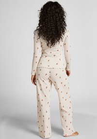 Romantische pyjama's van een gestructureerde stof in een crème kleur, met een bloemenpatroon in oranje en rood. De set bestaat uit een aansluitend langemouwen bovenstuk en relaxte, wijde broekspijpen.