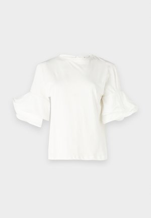 Hvit kortermet topp med rund hals og flagrende volangermer. Laget av lett bomullsblanding, med en jevn tekstur.