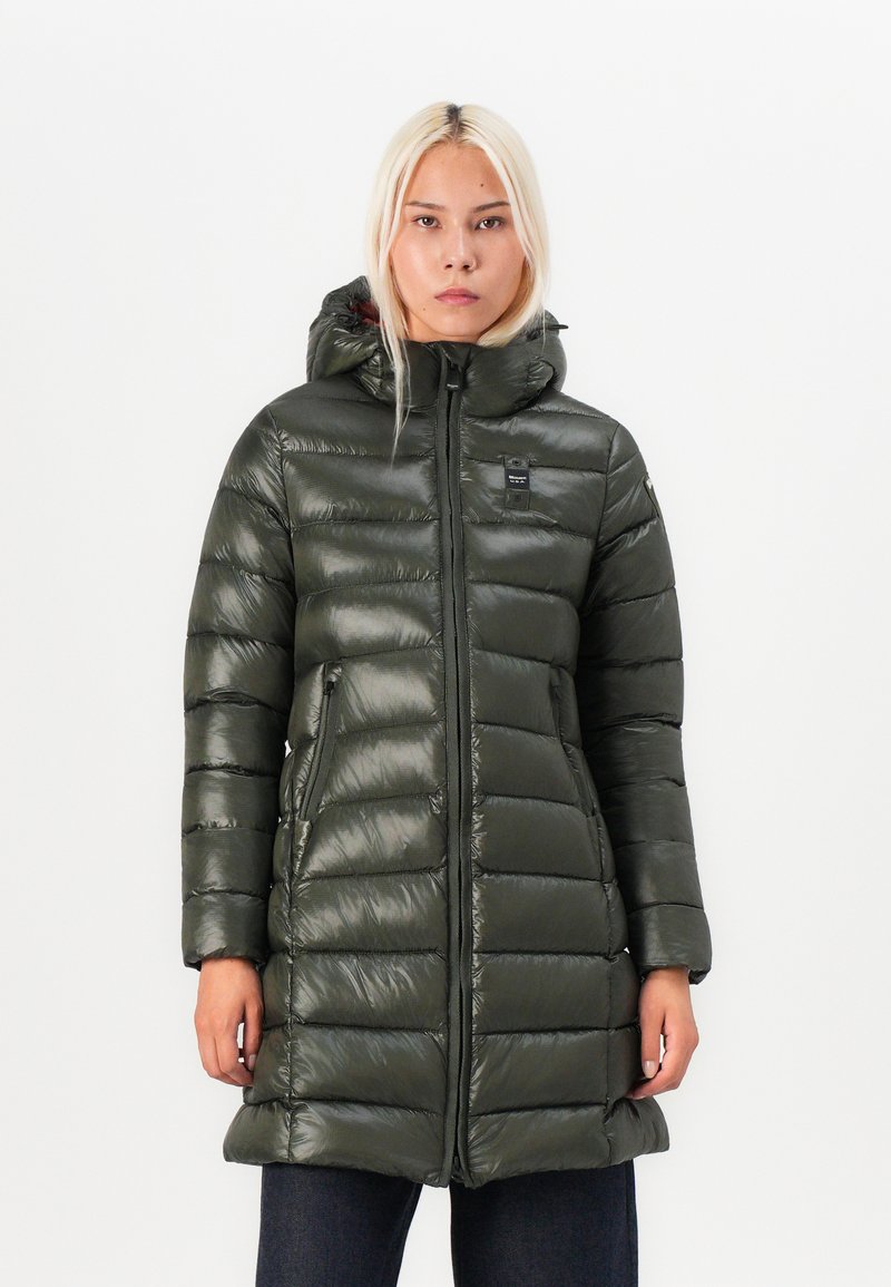 Kapsička s kapucňou v tmavozelenej farbe. Obsahuje lesklý materiál, vertikálny prešívaný vzor, plný zips a dve bočné vrecká.