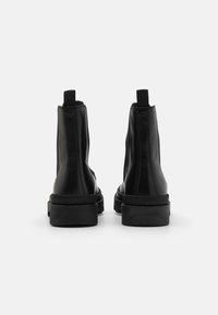 Bottines noires avec une texture en cuir lisse, des panneaux élastiques sur les côtés et une semelle en caoutchouc épaisse. Boucles à l'arrière pour un enfilage facile.