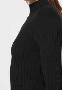 Pull noir à col roulé côtelé présentant des lignes verticales, une coupe ajustée et un col haut. Texture douce avec une légère élasticité.