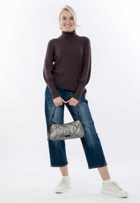 Bolso de mano gris acolchado con una correa corta, combinado con un suéter de cuello alto de canalé oscuro y pantalones vaqueros de mezclilla azul recortados. Las zapatillas blancas completan el look.