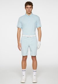Ljusblå polo med korta ärmar, matchad med ljusblå shorts. Vit bälte, vita handskar och vita sneakers med svarta ränder.