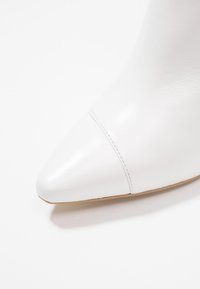 Białe skórzane botki za kostkę z ostrym noskiem i gładką teksturą. Posiadają detal szwu w okolicy noska oraz minimalistyczny design.