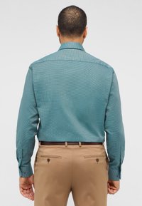 Teal mønstrede skjorte med knaplukning, lange ærmer og kontrasterende knapper, parret med tanfarvede dressbukser.