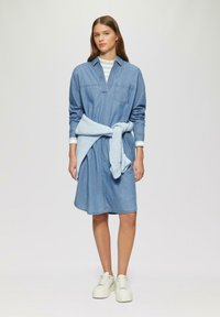 Denim šaty košeľového strihu s dlhými rukávmi, výstrihom do V a prednou kapsou, opásané svetlomodrým pleteným opaskom, skombinované s bielymi platformovými teniskami.