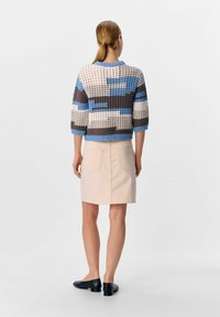 Gebreide trui met geometrische patronen in blauw-, bruin- en crèmekleuren; gecombineerd met een lichte roze spijkerrok; zwarte flats; casual outfit.