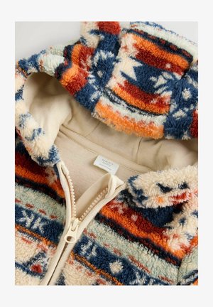 Krāsains fliša kapuci, ar ģeometrisku rakstu ziliem, oranžiem un krēmkrāsas toņiem, daļēji atpogāts, lai atklātu iekšējo audumu.