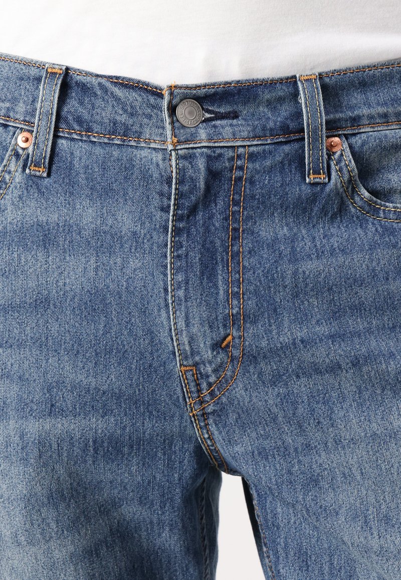 Jeans de mezclilla azul claro con costuras naranjas, que cuentan con un cierre de botón en la parte delantera, presillas para cinturón y diseño estándar de bolsillos.