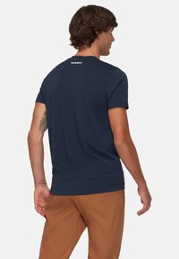 Donkerblauwe T-shirt met korte mouwen en een ronde hals, voorzien van een klein wit logo op de bovenrug; gemaakt van een zachte, lichte stof.