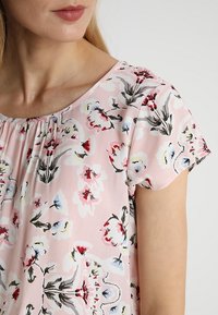 Top con stampa floreale a maniche corte, fondo rosa, presenta fiori rossi, blu e verdi, tessuto leggero, dettaglio con scollatura arricciata.