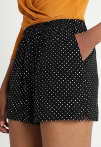 Černé kraťasy s puntíky, elastickým pasem, bočními kapsami a mírnými rozparky na lemu pro větší pohodlí a pohyb.