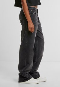 Zwarte wijde spijkerbroek in versleten denim met een hoge taille, voorzien van zijzakken en een contrasterend logo-label op de achterkant.