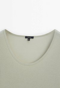 Haut en tissu côtelé vert clair avec un col rond et une étiquette de marque noire cousue à l'intérieur du col.