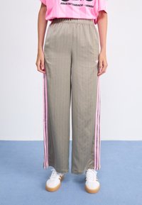 Ljusgrå, randiga träningbyxor med rosa sidorand och elastisk midja. Kombinerat med vita sneakers med gummisulor.