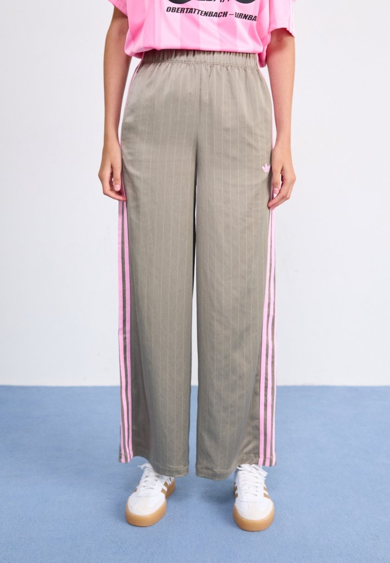 Ljusgrå, randiga träningbyxor med rosa sidorand och elastisk midja. Kombinerat med vita sneakers med gummisulor.