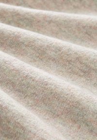 Gros plan d'un tissu en laine beige doux avec une texture tissée subtile et des plis délicats créant de légères ombres.