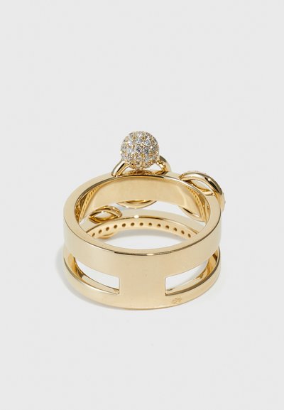 Gold ring featuring a circular, diamond-studded top. The band has cut-out sections and a smooth finish, with a polished texture throughout.