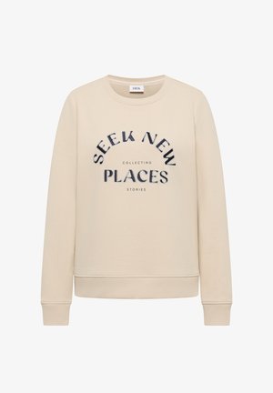 Beżowa bluza z prążkowanymi mankietami i ściągaczem u dołu, z czarnym napisem: "SEEK NEW PLACES" oraz mniejszymi słowami "COLLECTING STORIES" poniżej.
