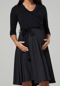 Vestido negro tipo envoltura con mangas tres cuartos, falda de lunares y un lazo en la cintura, hecho de una tela suave y elástica.
