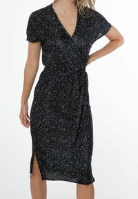 Svart midi-klänning med korta ärmar, prydd med vertikala vita ränder och en sidoklyvning. Knytning i midjan betonar formen. Mjuk tyg.