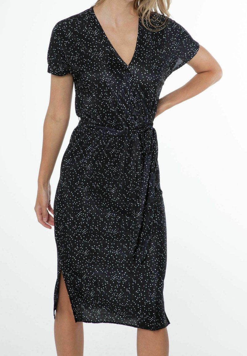 Svart midi-klänning med korta ärmar, prydd med vertikala vita ränder och en sidoklyvning. Knytning i midjan betonar formen. Mjuk tyg.