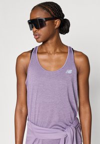 Μωβ αθλητική φανέλα με υφή, με ένα μικρό λογότυπο στο στήθος. Ορατοί μαύροι ιμάντες αθλητικού σουτιέν από κάτω.