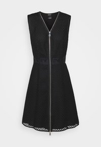 Robe noire sans manches en tissu texturé, dotée d'une fermeture éclair frontale et d'une large ceinture avec le logo DKNY. Silhouette trapèze avec ourlet ouvert.