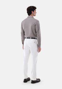 Camicia grigia a maniche lunghe con polsini abbottonati, abbinata a pantaloni bianchi e scarpe nere. La camicia presenta una leggera texture e un design del colletto classico.