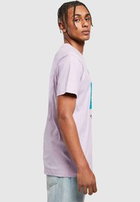 Lyse lilla bomulds-t-shirt med korte ærmer, prydet med et blåt grafikdesign på forsiden og diskrete tekstakcenter.