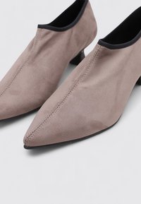 Botas de tobillo de ante gris con punta afilada, tacones bajos y detalles en negro alrededor de las aberturas. Presentan un diseño con costuras mínimas.
