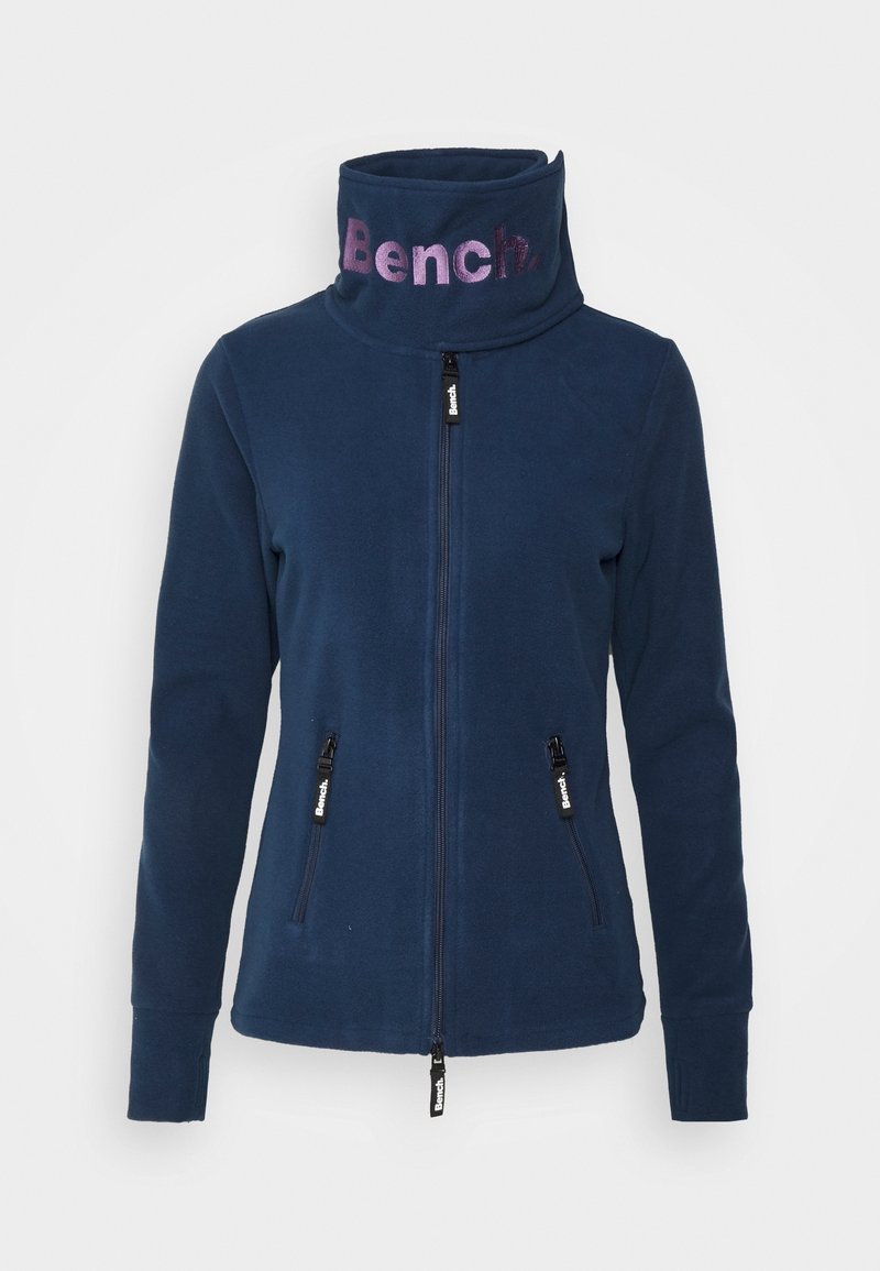 Veste polaire bleu marine zippée avec col montant affichant le logo "Bench" en violet, avec des poches latérales zippées et des tirettes de fermeture éclair de marque.