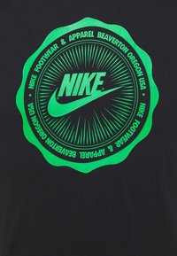 Černé tričko s velkým zeleným kruhovým logem s vyzařujícími linkami. Logo obsahuje název "Nike" a stylizovaný design swoosh.