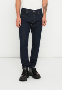 Jeans din denim de culoare albastră închisă, cu o croială slim, design cu cinci buzunare, cusături în contrast și închidere cu nasture metalic. Purtați cu pantofi negri.