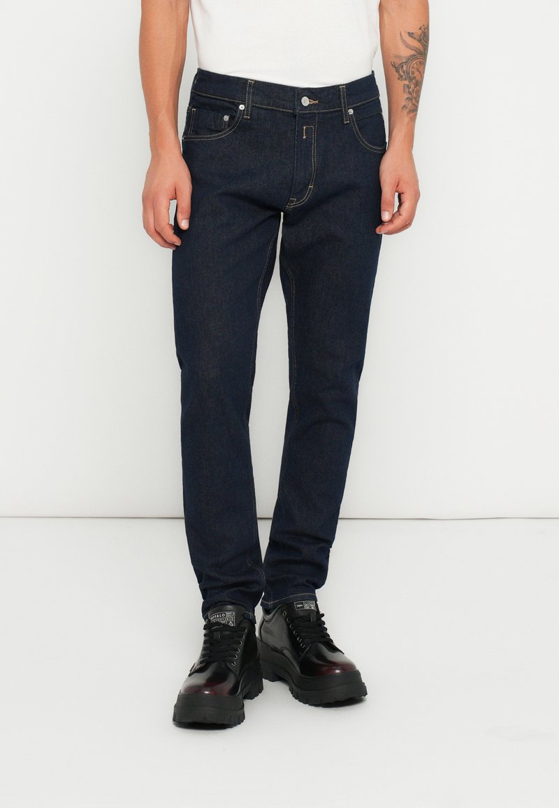 Jeans din denim de culoare albastră închisă, cu o croială slim, design cu cinci buzunare, cusături în contrast și închidere cu nasture metalic. Purtați cu pantofi negri.