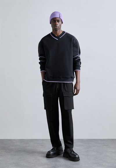 Felpa nera con accenti viola, scollo a V e vestibilità rilassata, abbinata a pantaloni cargo neri con tasche frontali e scarpe stringate nere.