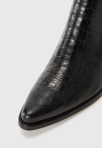 Bottine noire à talon avec un nez pointu, fabriquée en cuir texturé à motif crocodile, présentant un design épuré et de subtils détails de couture.
