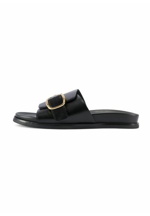 Czarna klapka na płaskiej podeszwie z szerokim paskiem z dużym złotym klamrą na białym tle.