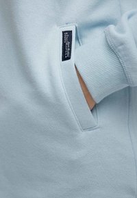 Sudadera azul claro con una textura suave, que cuenta con un bolsillo lateral y puños acanalados. Incluye una pequeña etiqueta de la marca en el bolsillo.