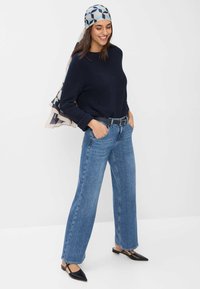 Marineblauwe gebreide trui, lichtblauwe hoge jeans met wijde pijpen, zwarte slingback schoenen en een patroonsjaal met geometrische ontwerpen.