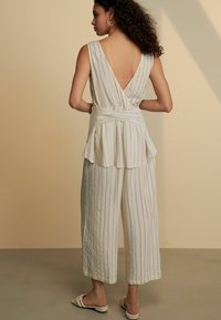 Lätt, randig jumpsuit i krämfärg med djup V-rygg, peplumdetalj och vida byxor. Har mjukt, strukturerat tyg.