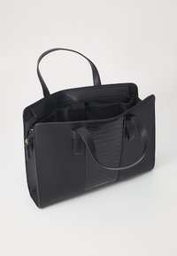 Sac fourre-tout noir en matériau synthétique avec un motif crocodile texturé sur un côté, anses doubles et une poche zippée intérieure.