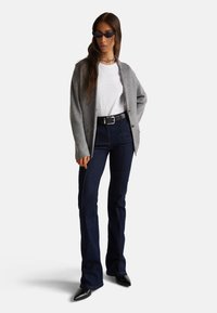 Šedý pletený cardigan přes bílé tričko, skombinovaný s tmavomodrými zvonovými džíny a špičatými černými lodičkami. Obsahuje stříbrný řetízek a sluneční brýle.