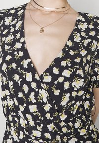 Robe florale noire ornée de petites fleurs blanches et jaunes, avec un décolleté en V profond, des manches courtes et un design noué. Tissu texturé.