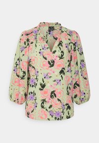 Blouse florale vert clair, ornée de roses roses et d'accents violets. Manches bouffantes, col froncé et tissu doux avec un léger éclat.