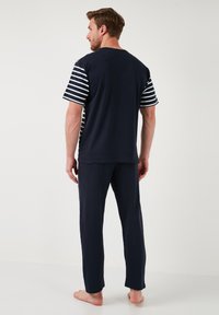 Marine lounge set met een effen kleur bovenstuk en gestreepte korte mouwen, vergezeld van bijpassende marineblauwe broeken. Gemaakt van zachte stof met een ontspannen pasvorm.