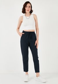 Námornícke jogger nohavice s elastickým pásom a šnúrkou, skombinované s bielym rebrovaným crop topom. Tenisky sú biele, materiál vyzerá hladko.